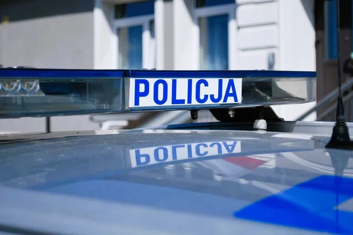 Lampa sygnalizacyjna z napisem POLICJA na dachu policyjnego pojazdu, w tle budynek.