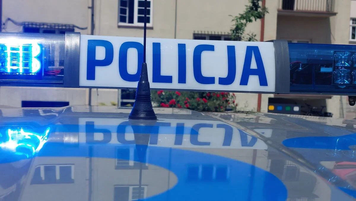 Lampa błyskowa z napisem POLICJA na dachu policyjnego radiowozu, w tle budynek mieszkalny.