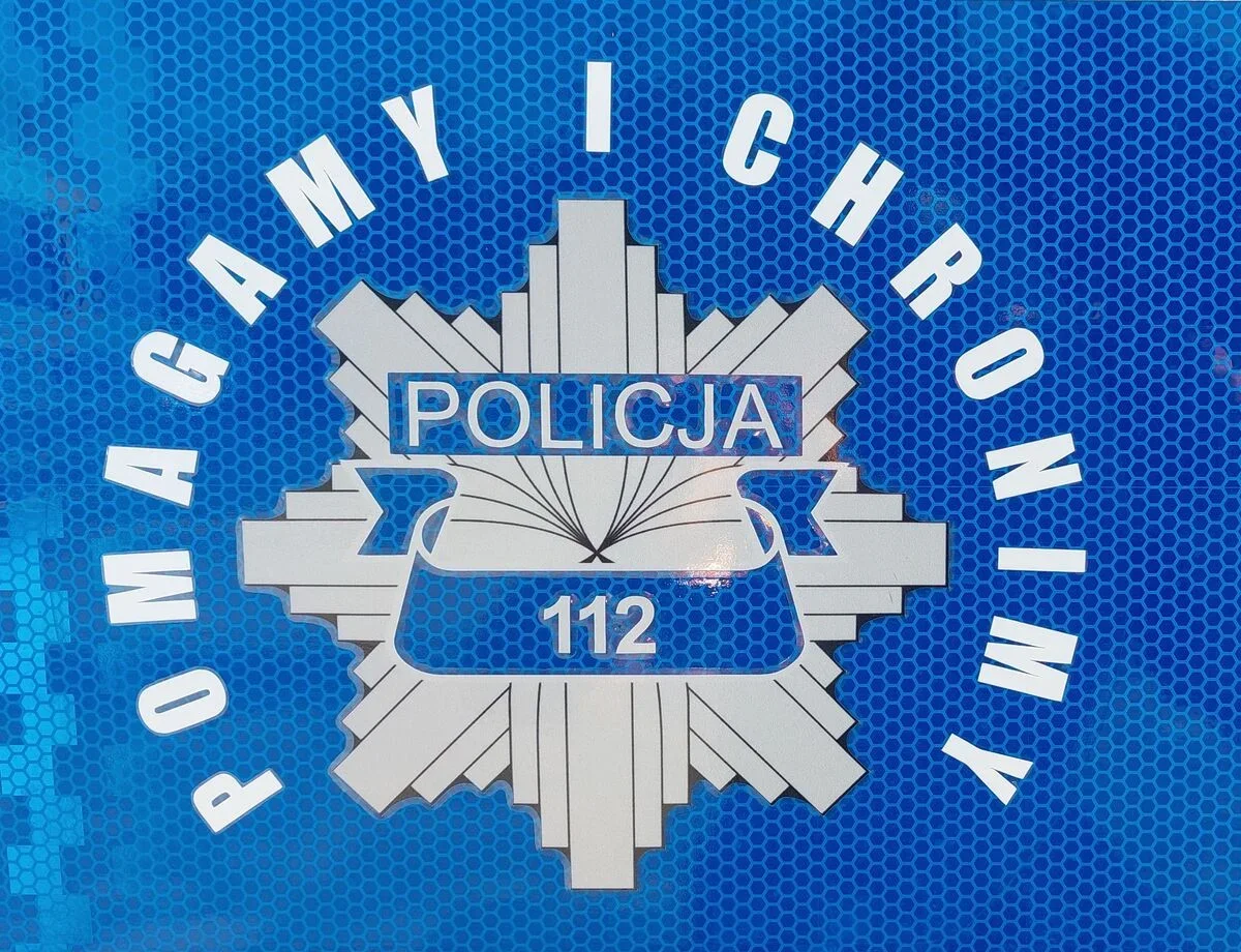 Fragment niebieskiego, odblaskowego oznakowania policyjnego z napisem „POMagamy i chronimy”, „POLICJA” i numerem alarmowym 112.