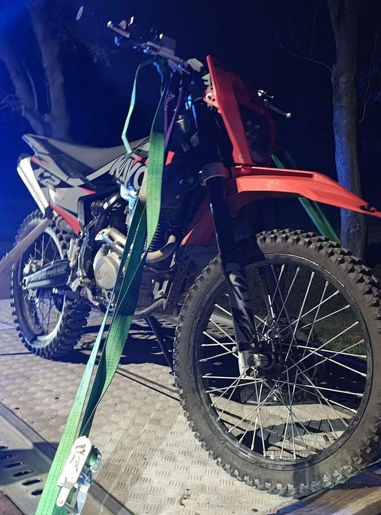 Czerwono-czarny motocykl crossowy przymocowany zielonym pasem do platformy w nocy.