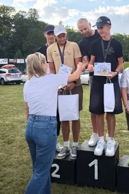 Kobieta wręcza dyplomy i upominki młodym mężczyznom stojącym na podium podczas ceremonii nagród na świeżym powietrzu.