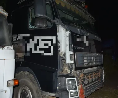 Uszkodzona ciężarówka Volvo stoi nocą na polanie, widoczne są zniszczenia przedniej części pojazdu obok innej ciężarówki.