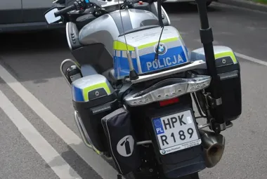 Tył policyjnego motocyklu BMW oznaczonego „POLICJA” stoi na drodze, na motocyklu widoczna polska rejestracja HPK R189 oraz napis reklamowy dealera.