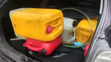 W bagażniku samochodu przewożone są plastikowe kanistry z płynami oraz węże.