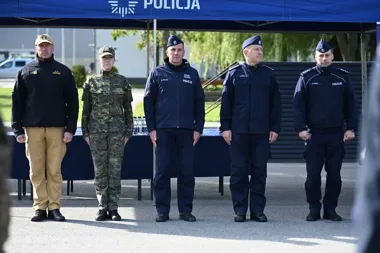 Pod namiotem z napisem POLICJA stoją w szeregu dwie osoby w mundurach wojskowych i trzej policjanci w granatowych mundurach.