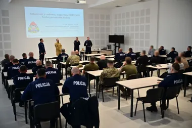 Funkcjonariusze Policji w sali szkoleniowej uczestniczą w wykładzie o zagrożeniach CBRN prowadzonym przez instruktorów.