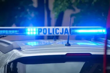 Fragment policyjnego radiowozu z włączonym niebieskim światłem na dachu, nocą.
