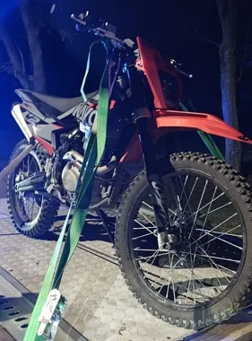 Czerwono-czarny motocykl crossowy przymocowany zielonym pasem do platformy w nocy.