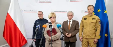 Cztery osoby, w tym funkcjonariusze służb mundurowych i osoba cywilna, stoją podczas konferencji prasowej przed flagami Polski i UE oraz banerem Wojewody Podkar