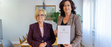 Dwie kobiety w biurowym wnętrzu, jedna z nich trzyma dokument z napisem „Wojewoda Podkarpacki”.
