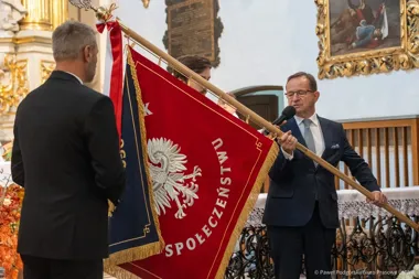 Mężczyzna w garniturze przemawia do mikrofonu podczas uroczystości wręczenia sztandaru w kościele.