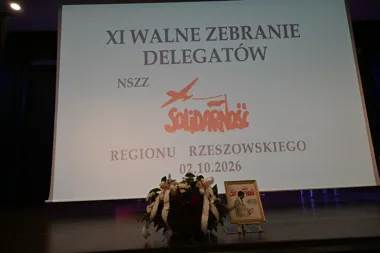 Ekran projekcyjny na scenie wyświetla planszę informacyjną XI Walnego Zebrania Delegatów NSZZ Solidarność Regionu Rzeszowskiego z datą 02.10.2026, przed ekranem