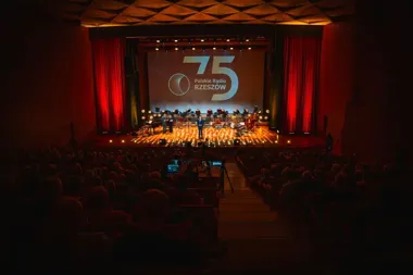 Widok z widowni na scenę koncertową z okazji 75-lecia Polskiego Radia Rzeszów, na której stoją prowadzący i widoczne są instrumenty muzyczne.